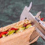 Using a vernier caliper to measure the width of a sandwich against a grey background